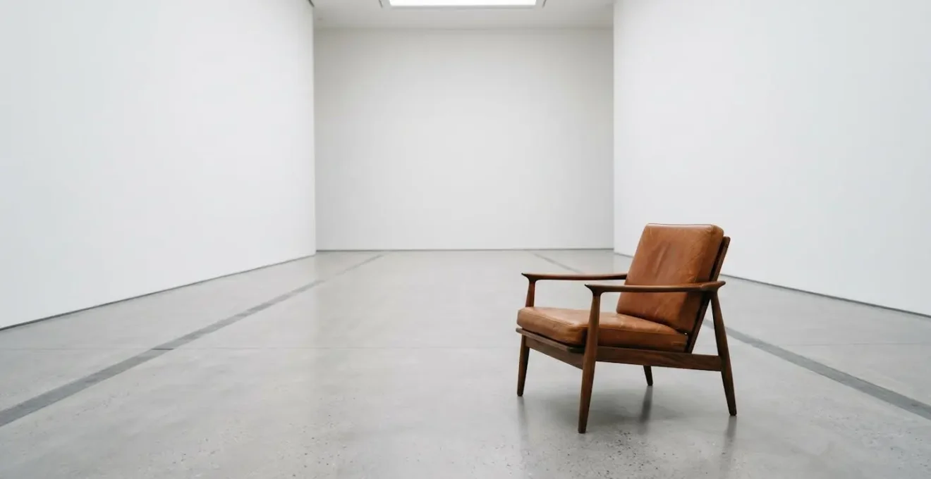Wide environmental shot of iconic mid-century chair in minimalist white gallery space with abundant negative space